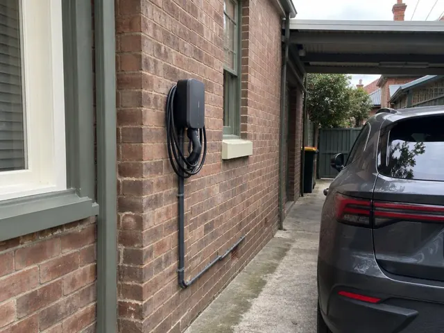 Wall-mounted EV charger on a brick exterior wall beside a driveway in Annandale