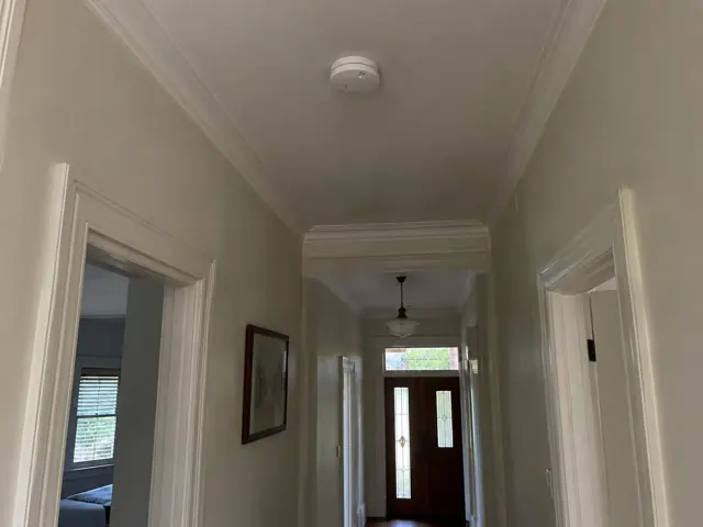 Ceiling smoke alarm in a narrow hallway with white trim and front door visible in Stanmore